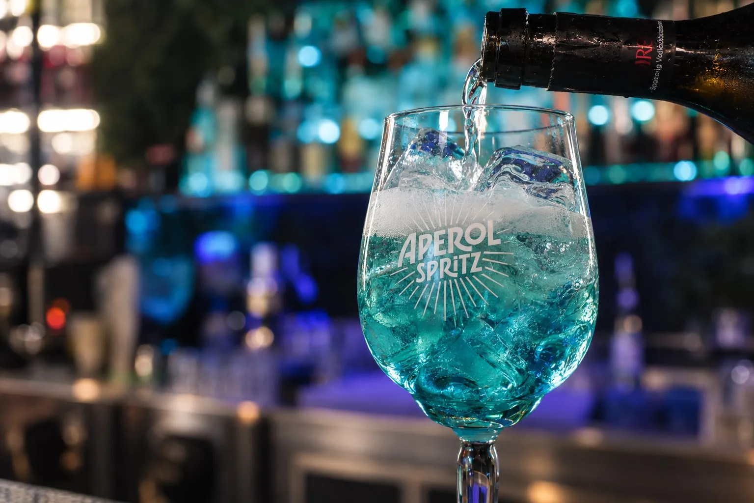Spritz versato nel bicchiere sul bancone, con le bottiglie illuminate dietro