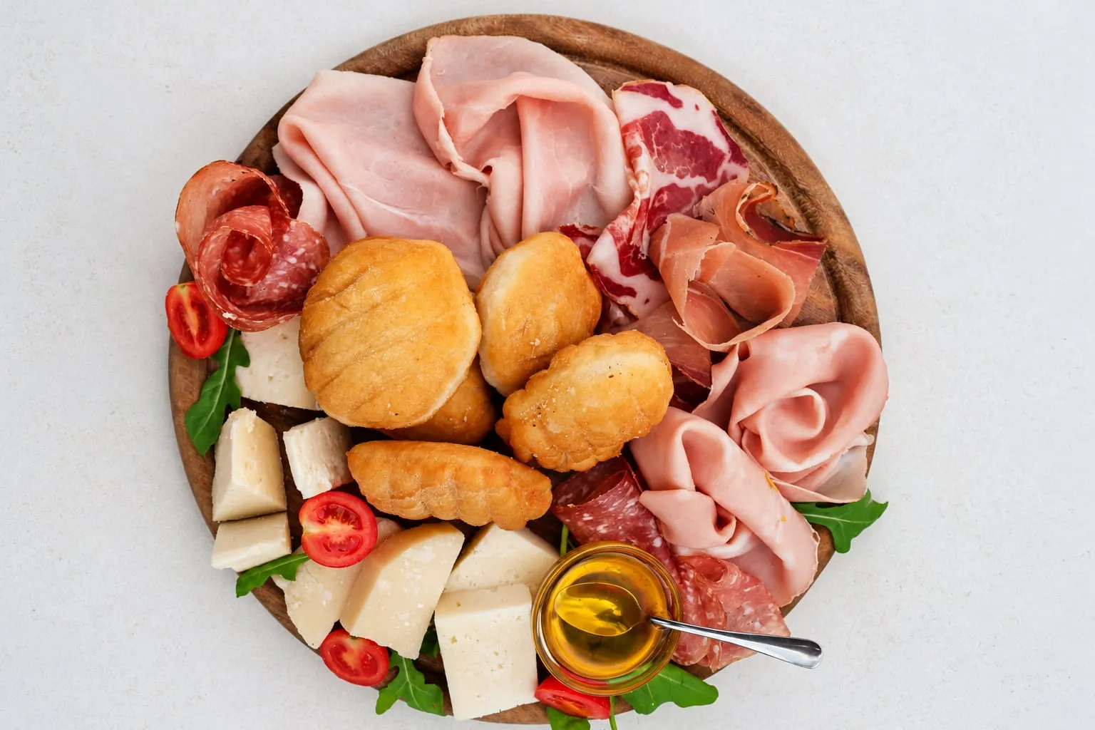 Tagliere visto dall’alto con gnocco fritto, salumi, formaggi, pomodorini e miele